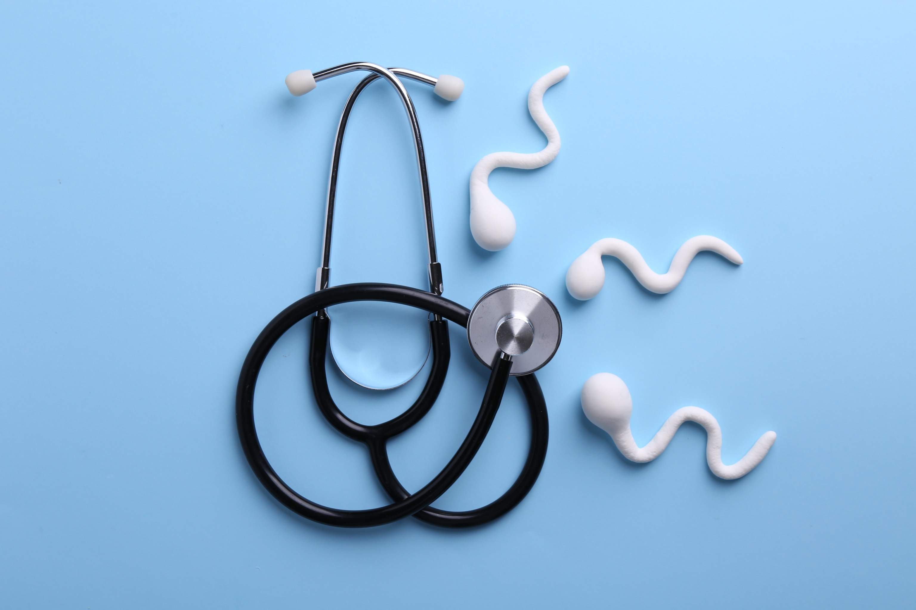 Figure of sperm cells and stethoscope on light blue background
