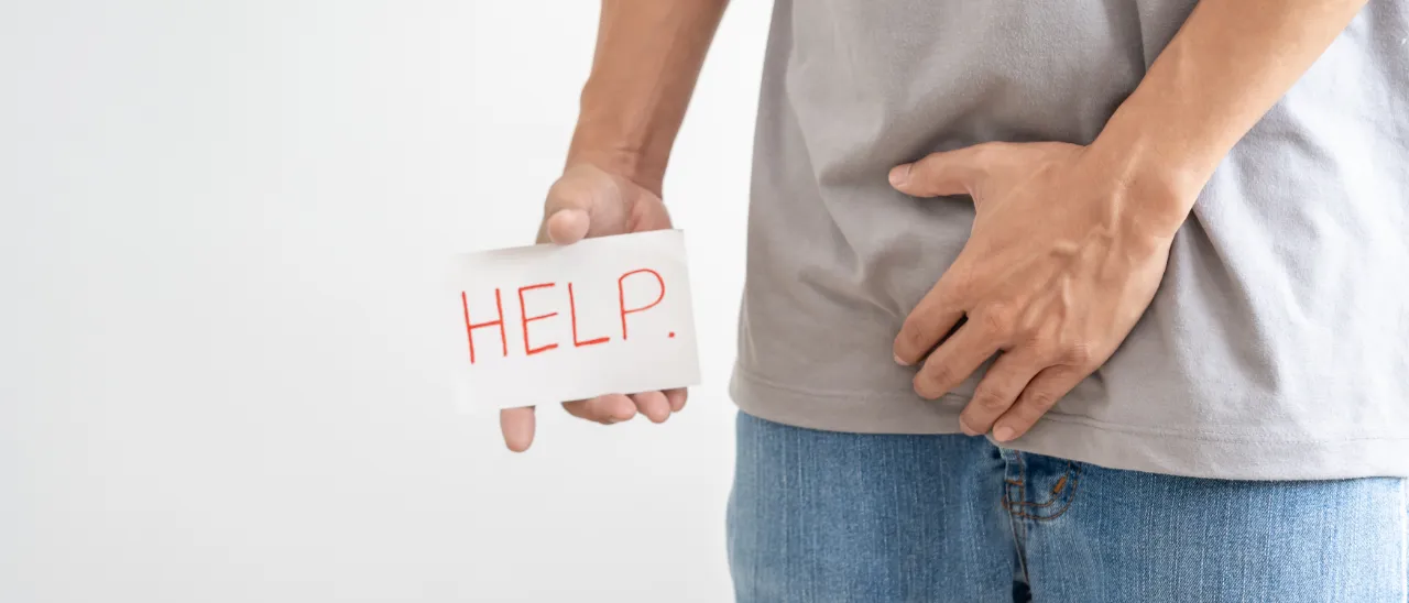 Man holding a 'HELP' sign while clutching his groin